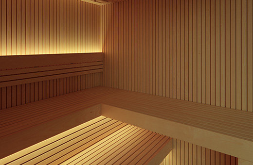Moderne Sauna für Zuhause, helles Saunaholz mit honigfarbenem Farbton und senkrechtem Linienverlauf der Innenverkleidung. Indirekte LED Beleuchtung der Rückenlehnen und der Saunabänke.